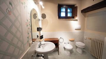 A bathroom with a sink, two toilets, a wooden cabinet, and a window with a view.