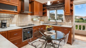A modern kitchen with wooden cabinets, stainless steel appliances, and a glass dining table. - Villa Ithaca.  Country side villa close to all worth visiting sights in Chania.  (CHANIA)