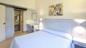 A hotel room with a bed, bedside tables, a desk, a chair, a bathroom, and a painting on the wall.