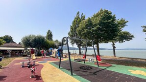 A playground with swings and slides, a covered seating area, and a view of the water.