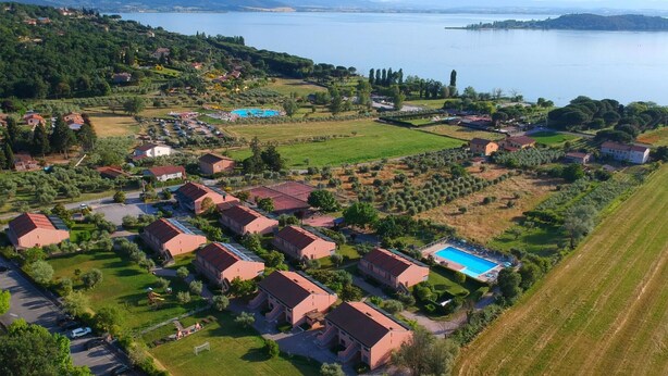 An aerial view of a residential area with houses, a swimming pool, and a large body of water in the background.