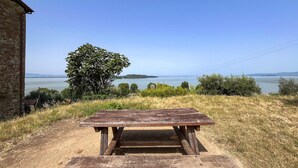 A rustic wooden picnic table in a grassy area with a view of a lake and distant hills.