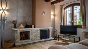 A living room with a stone fireplace, a television, and a window with curtains. - Quiet 4-bedroom house near Munts beach, air-conditioned, shared pool (Torredembarra)