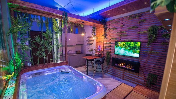 Un área de spa moderna con un jacuzzi, suelo de madera y una pantalla de televisión.