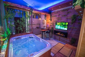Un área de spa moderna con un jacuzzi, suelo de madera y una pantalla de televisión.
