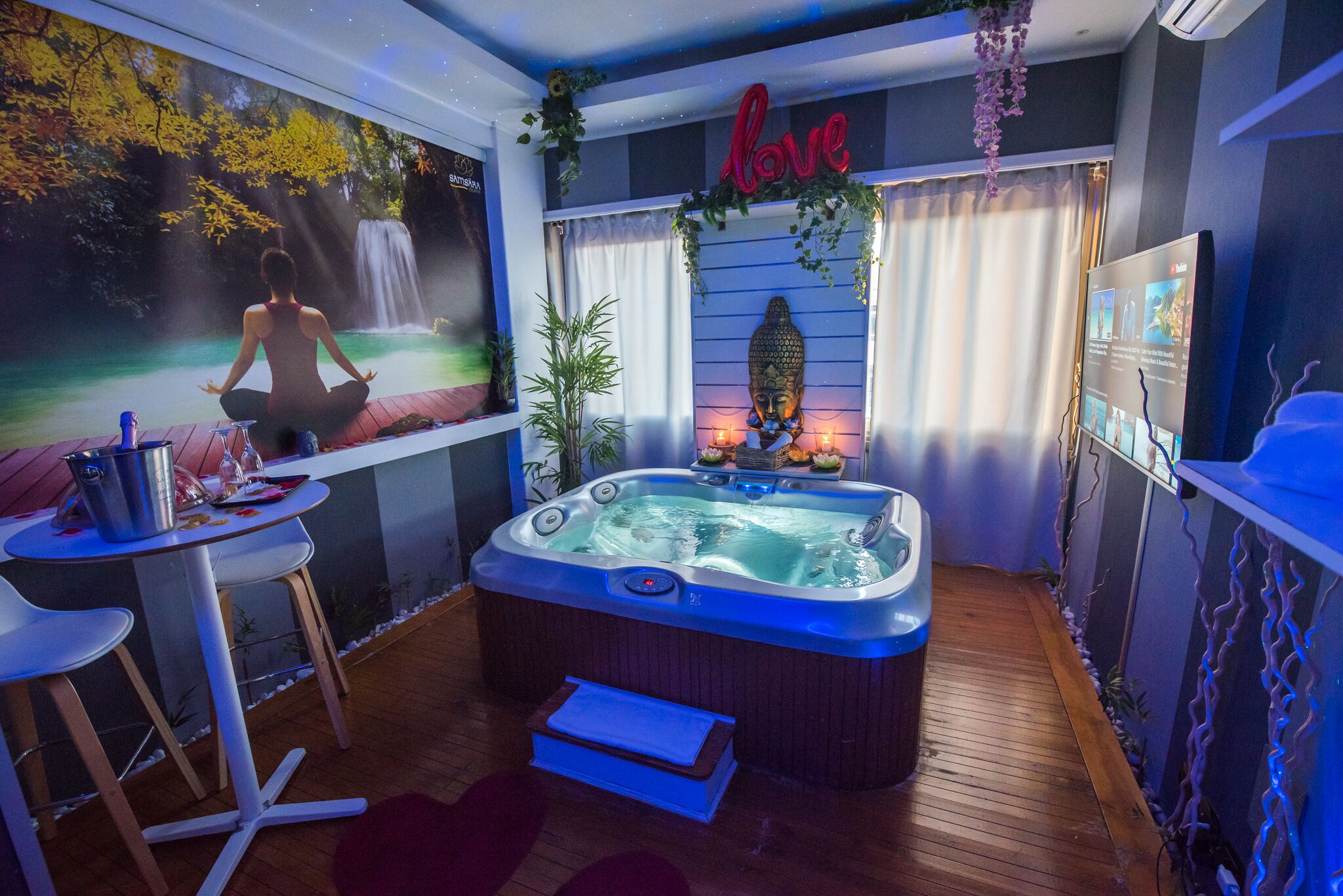 A spa room with a hot tub, a meditation area with a waterfall mural, and a 'love' sign above the hot tub.