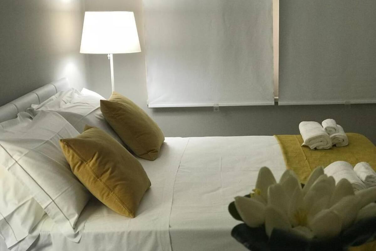Habitación de hotel con cama, almohadas, lámpara, ventana y toallas sobre una mesita.