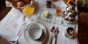 A breakfast setting with a glass of orange juice, a bowl, a plate with butter, jam, and a sugar bowl.