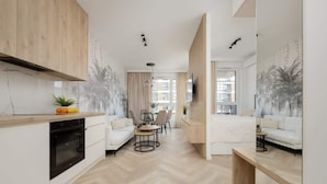 Un apartamento moderno con cocina, comedor y sala de estar. Destaca por su suelo con patrón de espiga, armarios de madera y un amplio ventanal que proporciona luz natural.