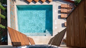Une piscine rectangulaire à l’eau claire, entourée d’une terrasse carrelée et de chaises longues en bois.