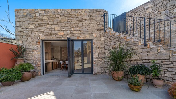 Un bâtiment en pierre avec une entrée dotée d’une porte en verre, des places assises à l’extérieur et des plantes en pot.