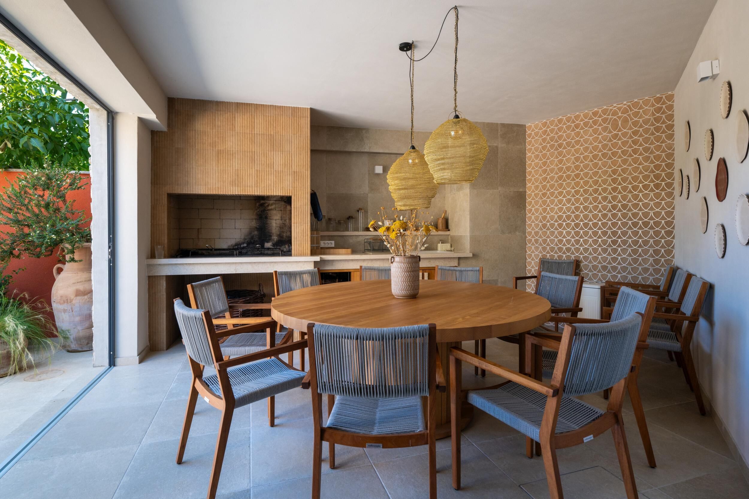 A modern kitchen with a round wooden table and six chairs, a hanging light fixture, and a patterned wall.