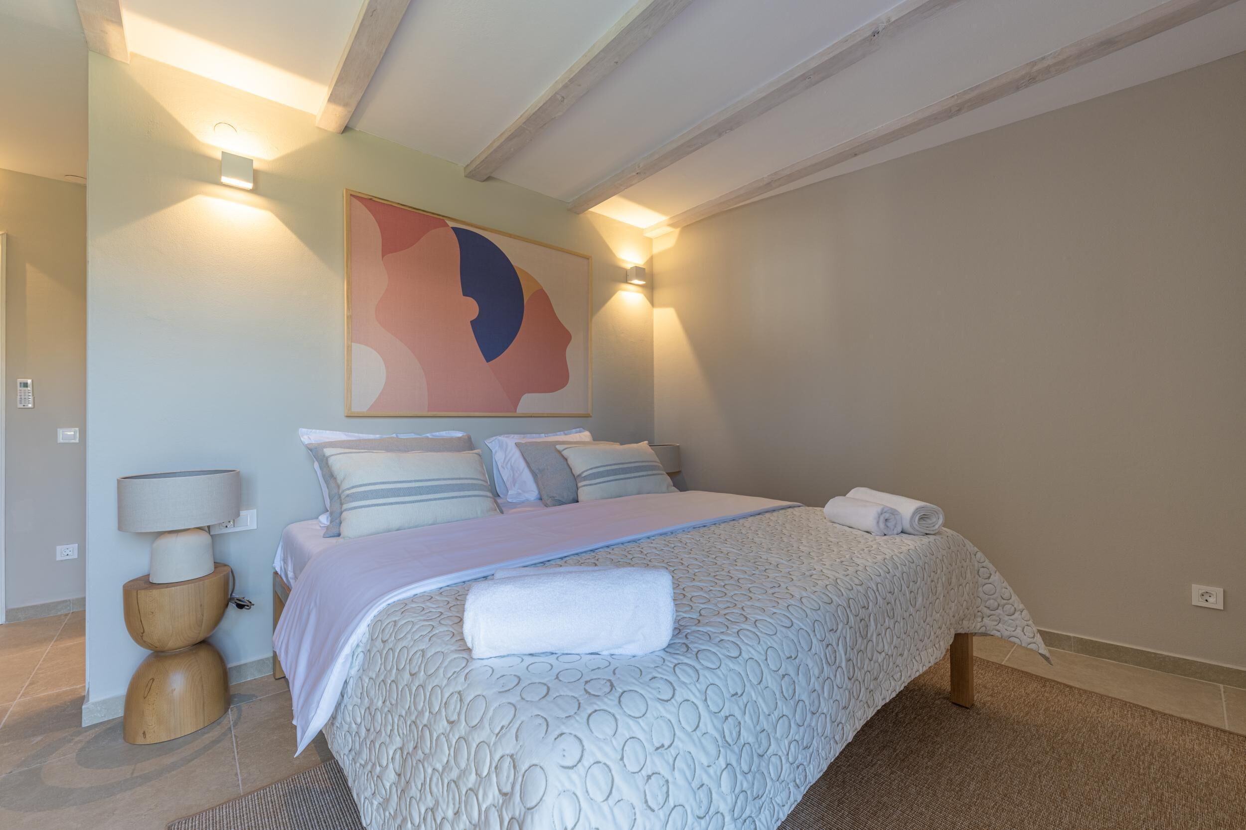 Een slaapkamer met een groot bed, twee bedlampen, een wandlamp en een groot abstract schilderij.
