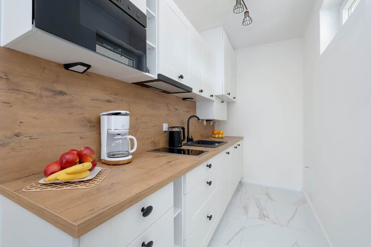 A modern kitchen with a wooden countertop, white cabinets, a coffee maker, and fruits.
