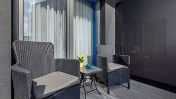 Ein Balkon mit zwei Korbstühlen und einem kleinen Tisch mit einem Blumenvasen.