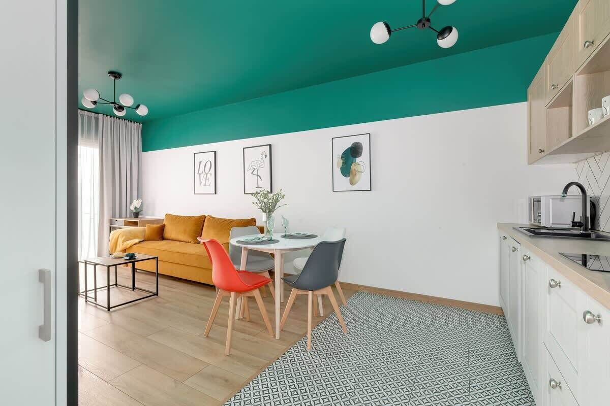 Ein modernes Wohnzimmer mit himbeerfarbener Decke, einem gelben Sofa, einem Esstisch mit Stühlen und einer Küchenzeile mit Schränken und Spüle.