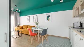 Ein modernes Wohnzimmer mit himbeerfarbener Decke, einem gelben Sofa, einem Esstisch mit Stühlen und einer Küchenzeile mit Schränken und Spüle.
