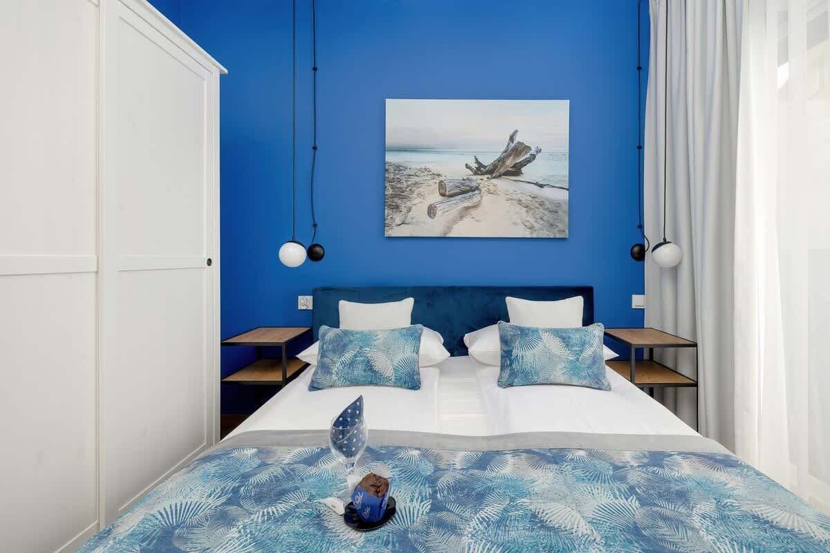 Une chambre avec un grand lit, deux tables de chevet, un mur bleu et un tableau sur le thème de la plage.