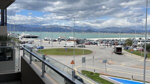 Blick vom Balkon auf einen belebten Kreuzungspunkt mit einer Marina, Fahrzeugen und Bergen im Hintergrund.