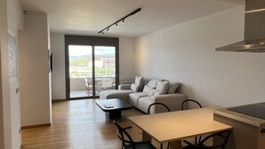 Ein modernes Wohnzimmer mit einer Couch, einem Esstisch und Stühlen. Ein Glastür öffnet sich zum Balkon mit Blick auf die Stadt.