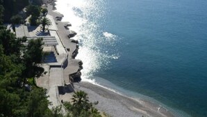 Eine Luftaufnahme einer Küstenregion mit einem gepflasterten Weg entlang des Strandes, einer felsigen Küstenlinie und etwas Grün.