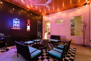 An outdoor seating area with wicker furniture, a checkered floor, a neon sign, and a fire pit. - Private Mini Golf and Covered Fireplace Lounge (Austin)