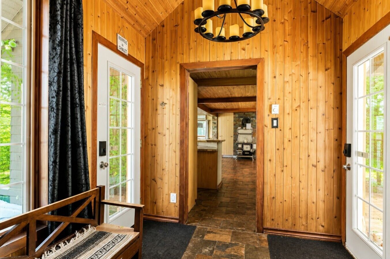 A wooden interior hallway leading to a kitchen area with a chandelier.