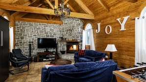 Een gezellige woonkamer met een stenen muur, een open haard, een televisie en een groot bord met de tekst 'JOY'.