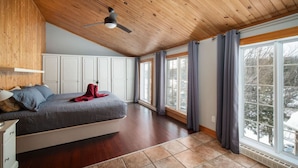 Een ruime slaapkamer met een groot bed, houten plafond en grote ramen.