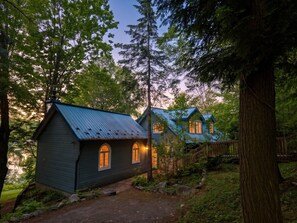 A cabin with a metal roof, surrounded by trees and a wooden fence.