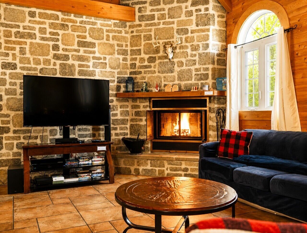 A cozy living room with a stone wall, a fireplace, a television, and a sofa.