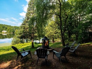 An outdoor seating area with Adirondack chairs and a fire pit, surrounded by trees and a lake. - Maison bord de Lac 1h de Mtl, Spa, Foyer (Saint-Calixte)