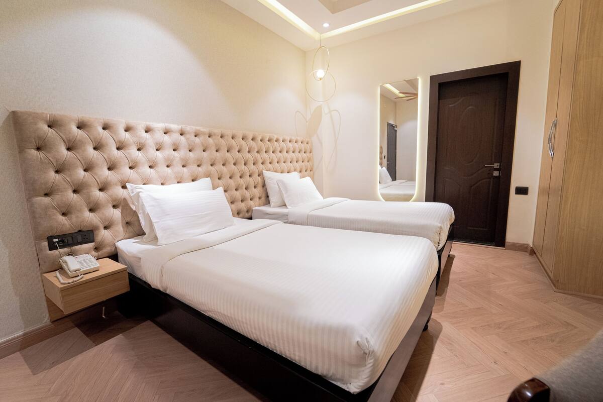 Une chambre d’hôtel dotée d’une grande tête de lit capitonnée, de deux lits, d’une table de chevet avec un téléphone et d’une armoire en bois.