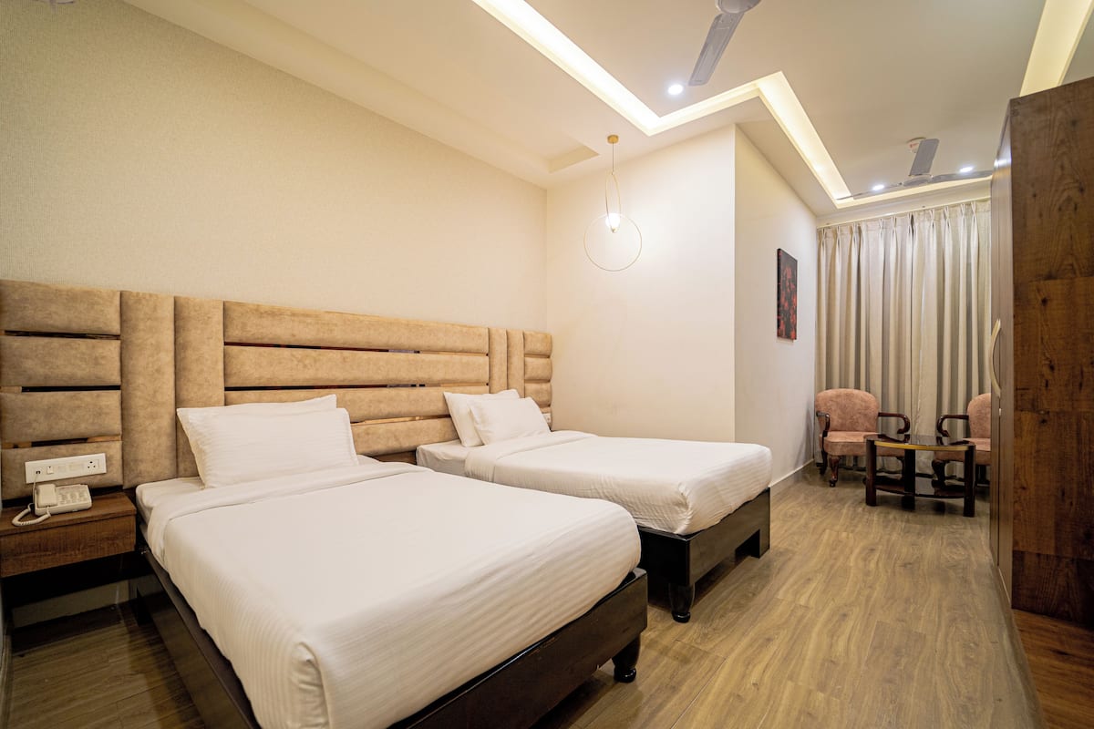 Une chambre d’hôtel avec deux lits, une tête de lit en bois, un bureau avec une chaise, un téléphone et un luminaire fixé au mur.