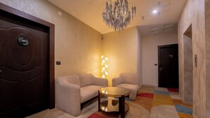 A modern hotel lobby with a sofa set, a round coffee table, a chandelier, and a colorful carpet. - Pink Mango A Boutique Hotel (Hisar)