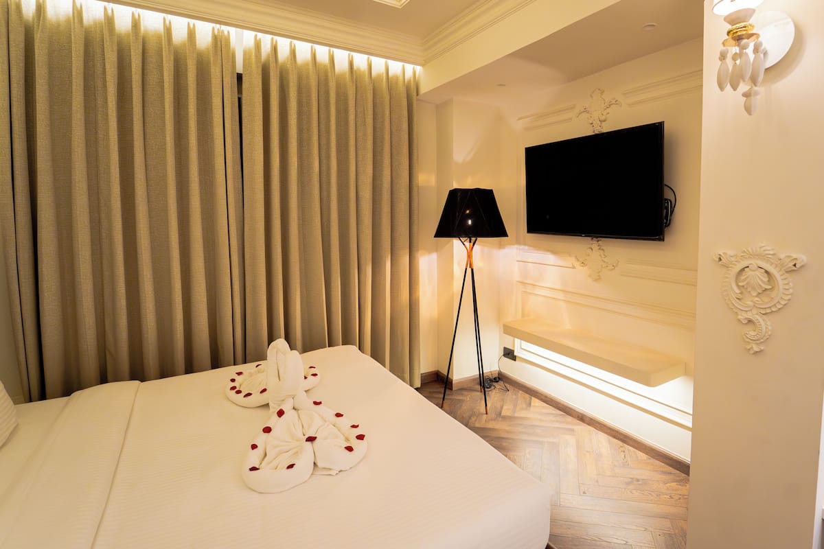 Une chambre d’hôtel comprenant un lit, des rideaux, un téléviseur à écran plat, une lampe et un luminaire fixé au mur.