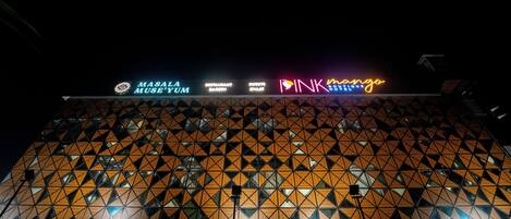 A building with a geometric facade and illuminated signage for MASALA MUSEUM, SWISS RESTAURANT, and INK Mango.