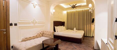 A hotel room with a sofa, a bed, a ceiling fan, and a small table.