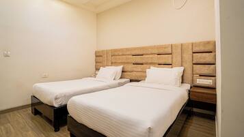 A hotel room with two single beds, wooden headboards, white bedding, and a small bedside table with a lamp.