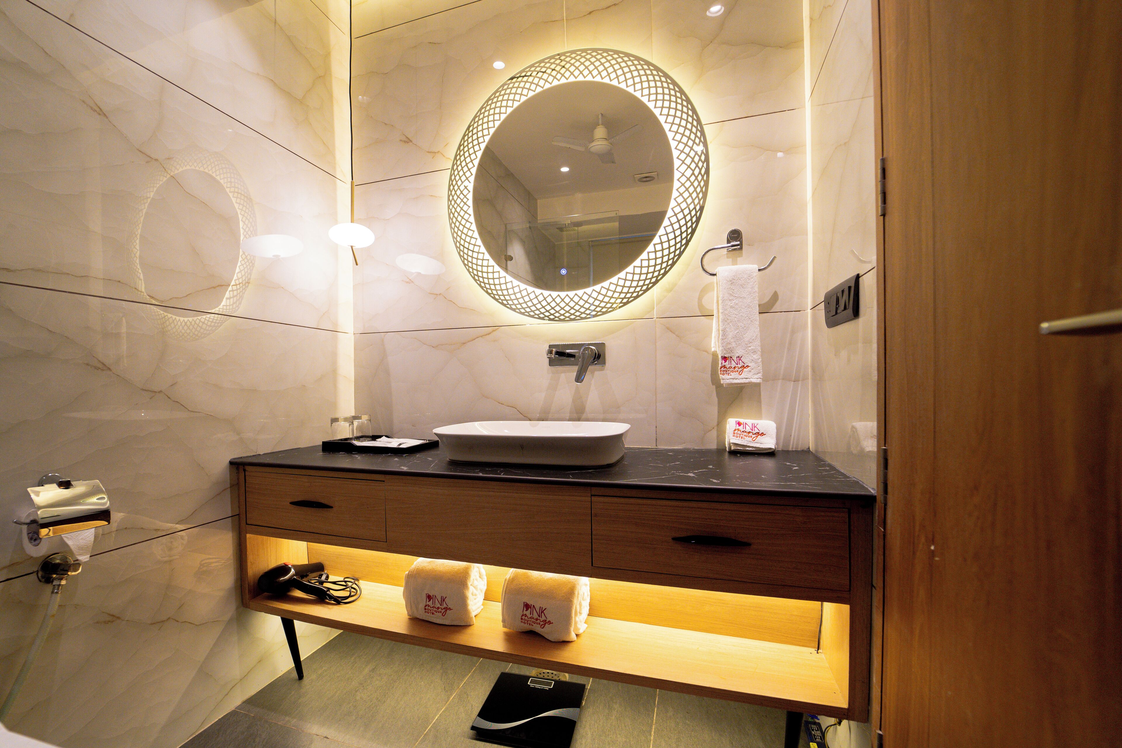A modern bathroom with a marble wall, a round mirror, a sink, and a towel rack.