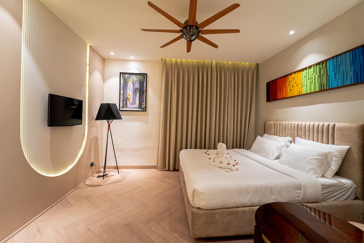 Une chambre d’hôtel moderne avec un grand lit, un ventilateur de plafond, un téléviseur à écran plat, un tableau et une œuvre d’art colorée accrochée au mur.