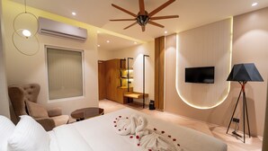 A modern hotel room with a bed, a seating area, a TV, and a ceiling fan. - Pink Mango A Boutique Hotel (Hisar)
