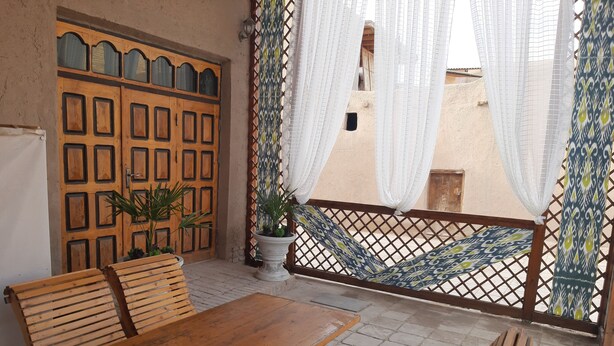 Une table et des bancs en bois sur une terrasse, avec une clôture à motifs et une grande porte en bois.