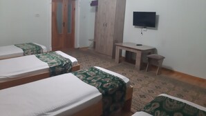 Une chambre avec trois lits, une armoire en bois, une télévision et une petite table.