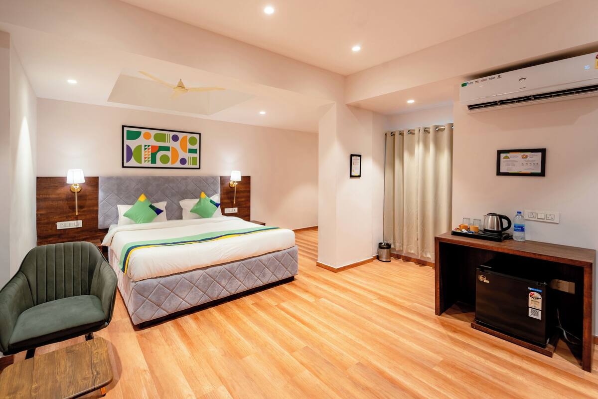 A hotel room with a bed, a chair, a desk, an air conditioner, and a ceiling fan.