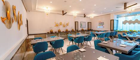 A modern dining area with blue chairs, tables set for meals, and decorative wall art.