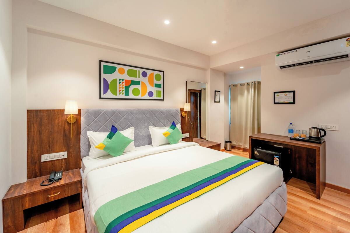A hotel room with a bed, bedside table, lamp, and a painting on the wall.