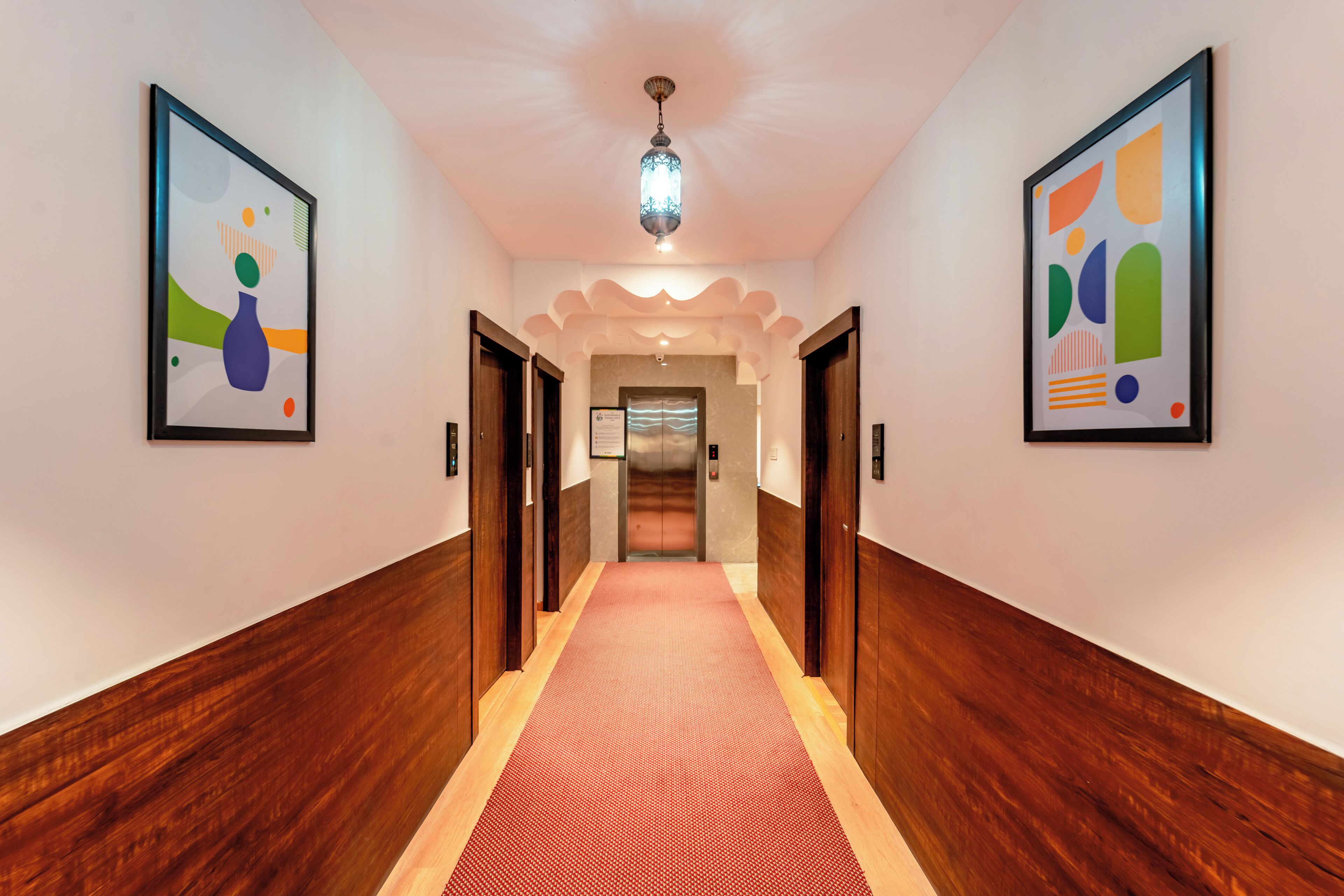 A hallway with a red carpet, wooden walls, and two framed abstract paintings.
