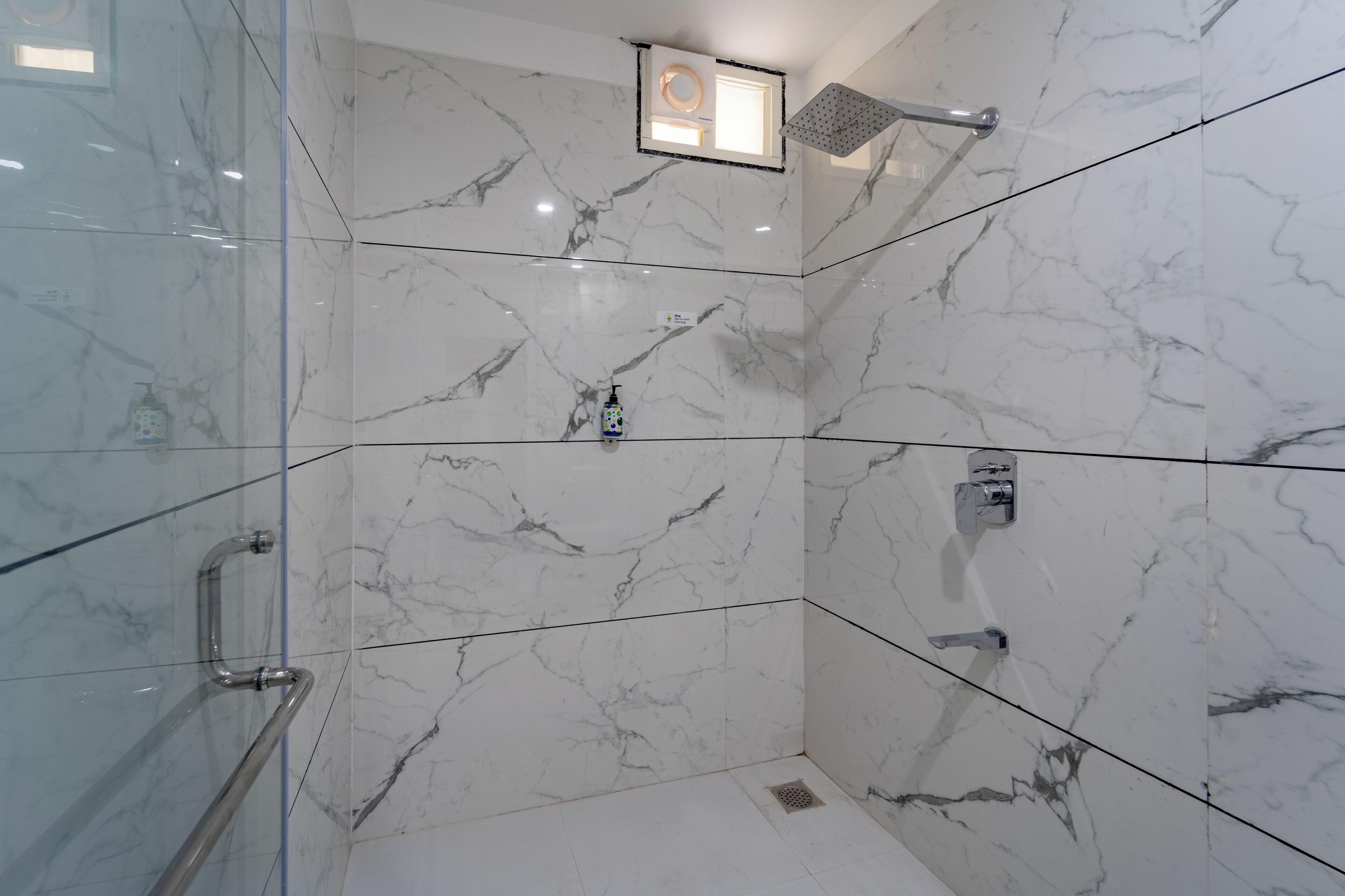 A modern bathroom with marble walls, a glass shower enclosure, and a handheld showerhead.