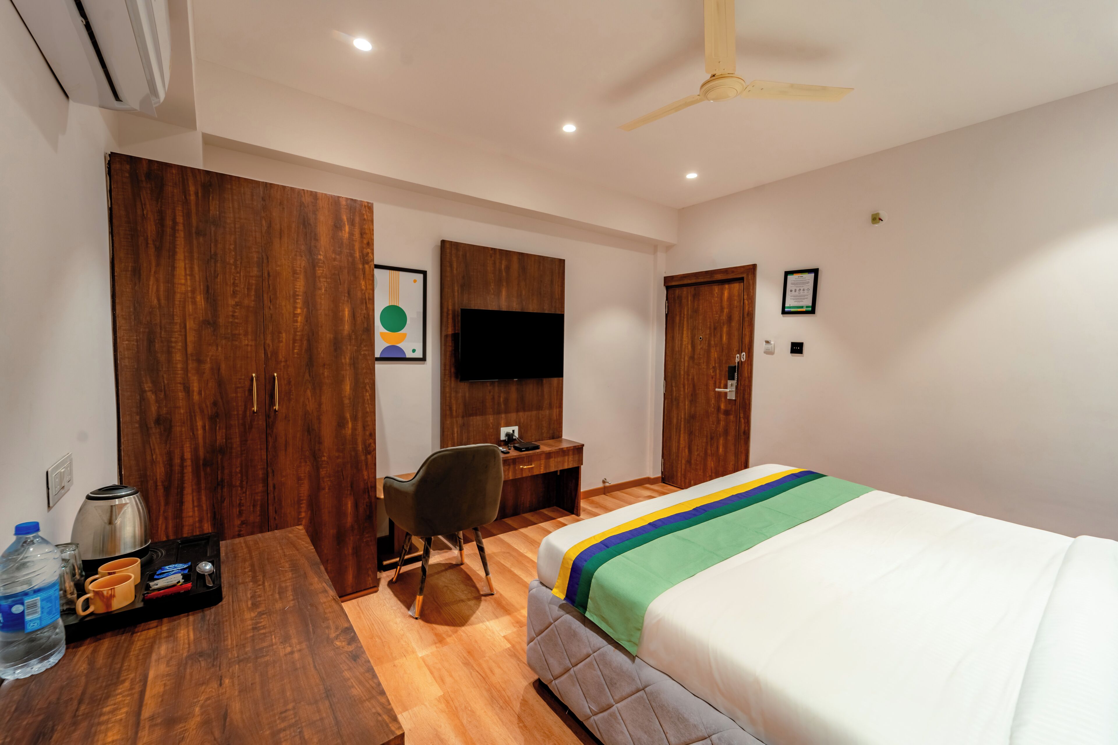 A hotel room with a bed, wooden wardrobe, desk, chair, and a television.
